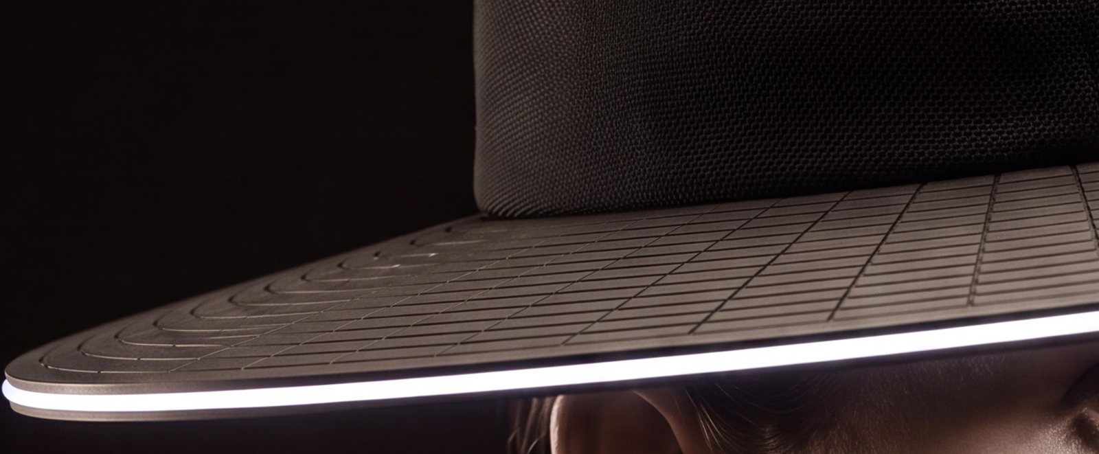 Close view of the brim's top surface: rings of long flat panels on straight joints, the knit crown above and the lit edge below.